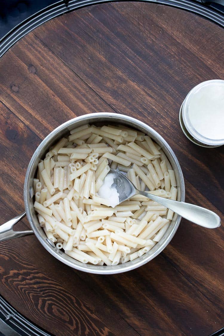 Spoon mixing coconut oil into a pot of penne pasta