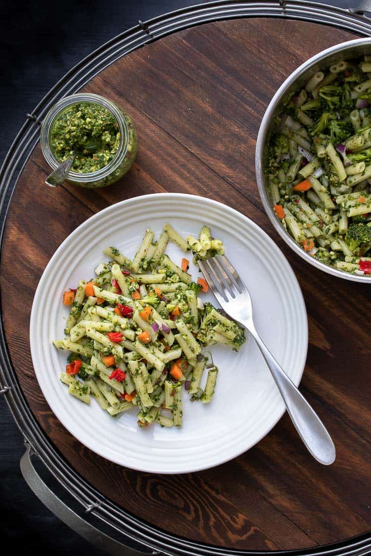 Pot of pesto pasta salad next to white plate filled with it