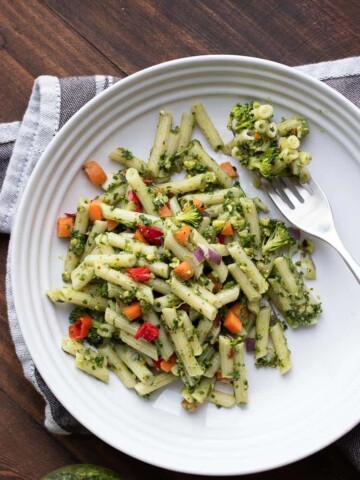 Vegan pesto pasta and veggies and a fork on a white plate