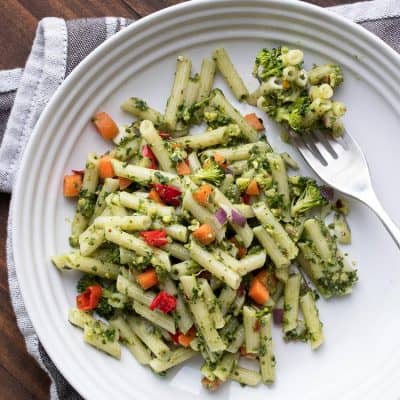 Vegan pesto pasta and veggies and a fork on a white plate