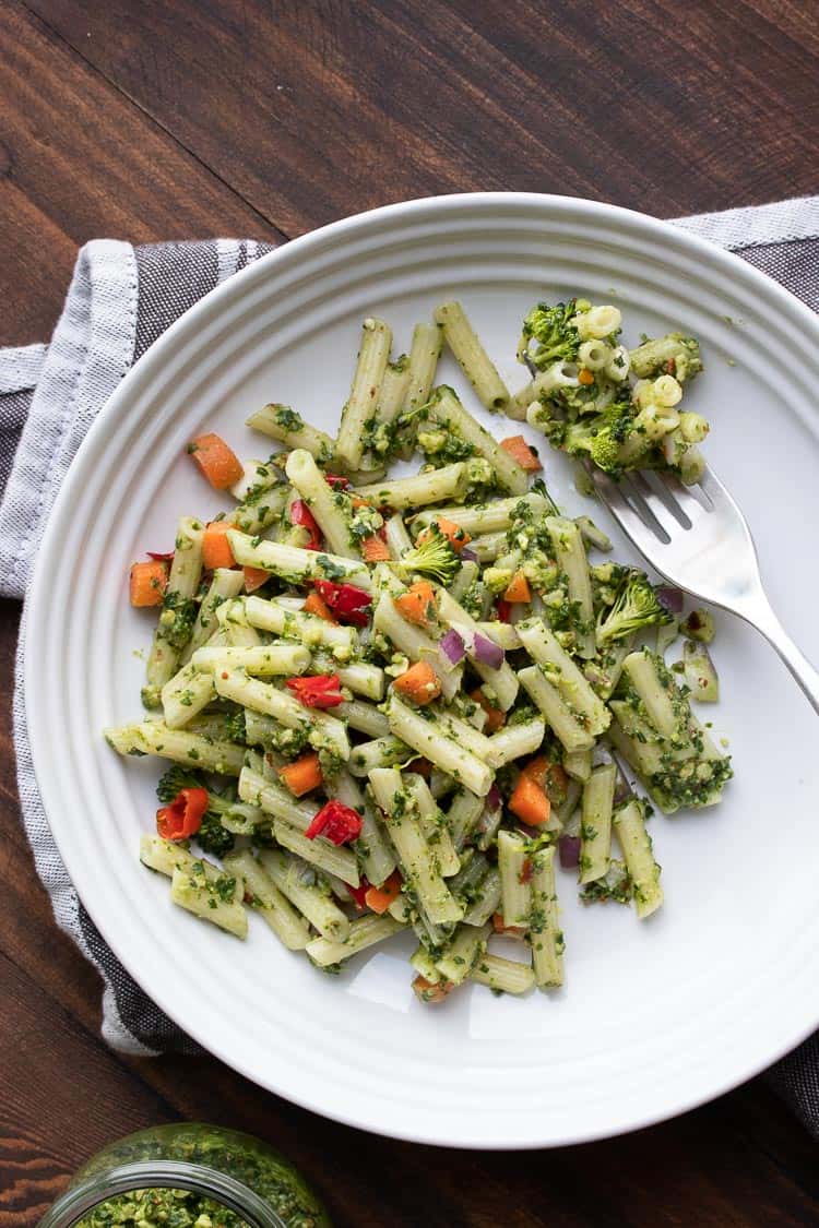 Vegan pesto pasta and veggies and a fork on a white plate