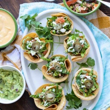 Top view of crunchy taco cups filled with toppings on a white platter