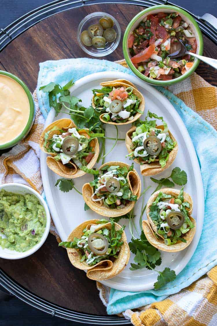 Top view of crunchy taco cups filled with toppings on a white platter