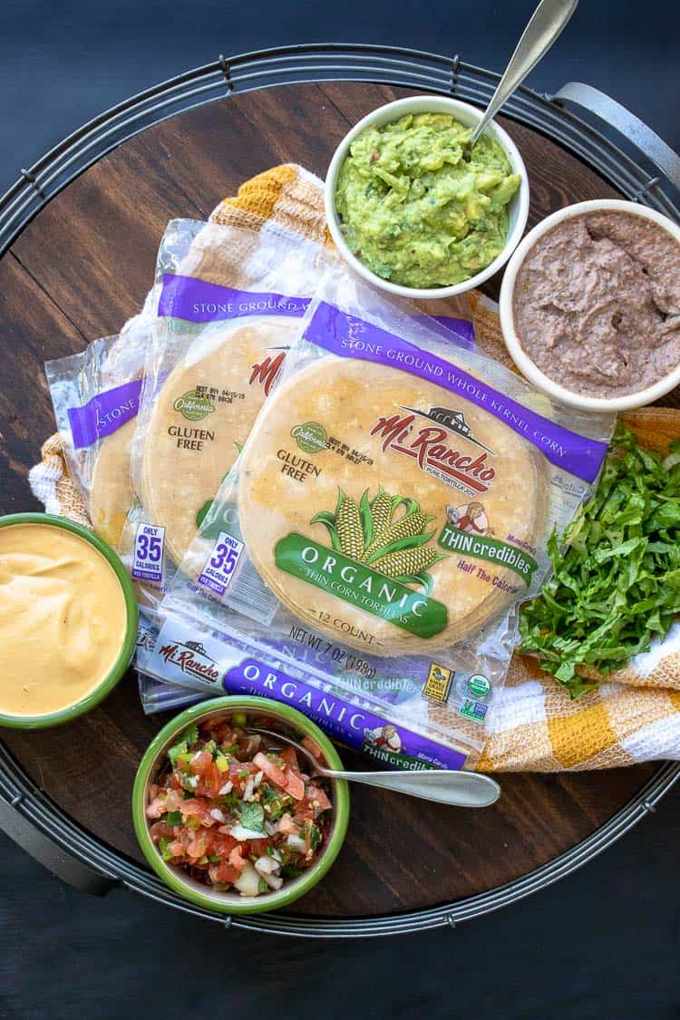 Tortilla packages surrounded by toppings on a wood tray