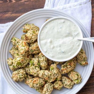 Broccoli tots on a white plate next to a bowl of creamy dip