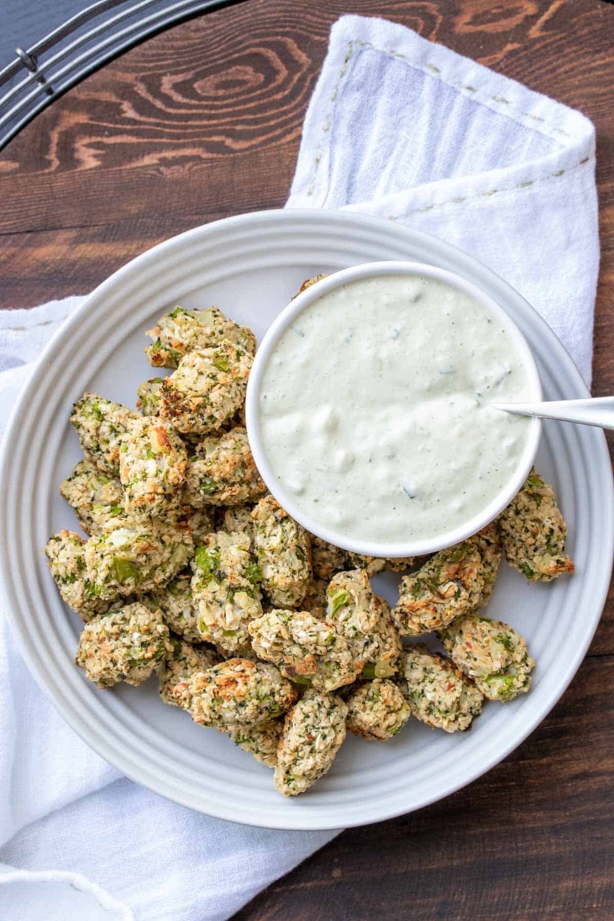 Broccoli tots on a white plate next to a bowl of creamy dip