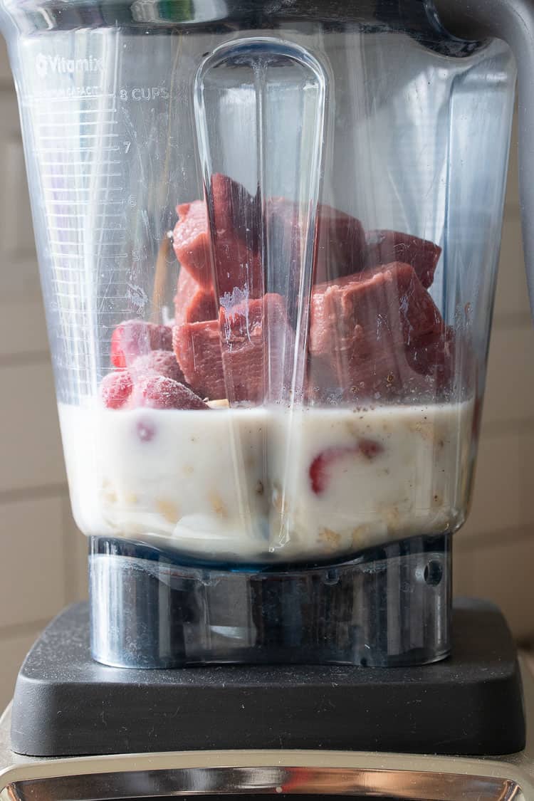 Blender with strawberry ice cubes, strawberries and milk