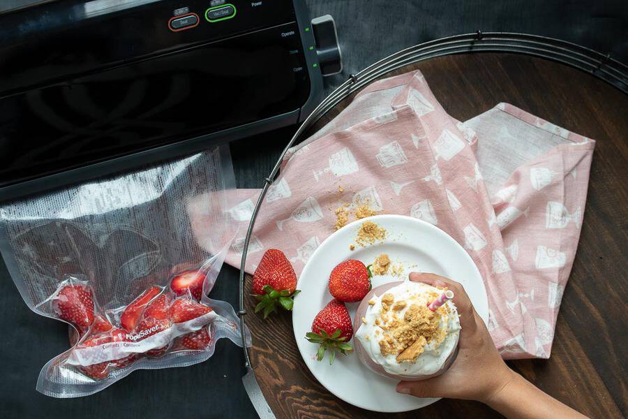 Top view of a hand taking a smoothie next to vacuum sealed strawberries