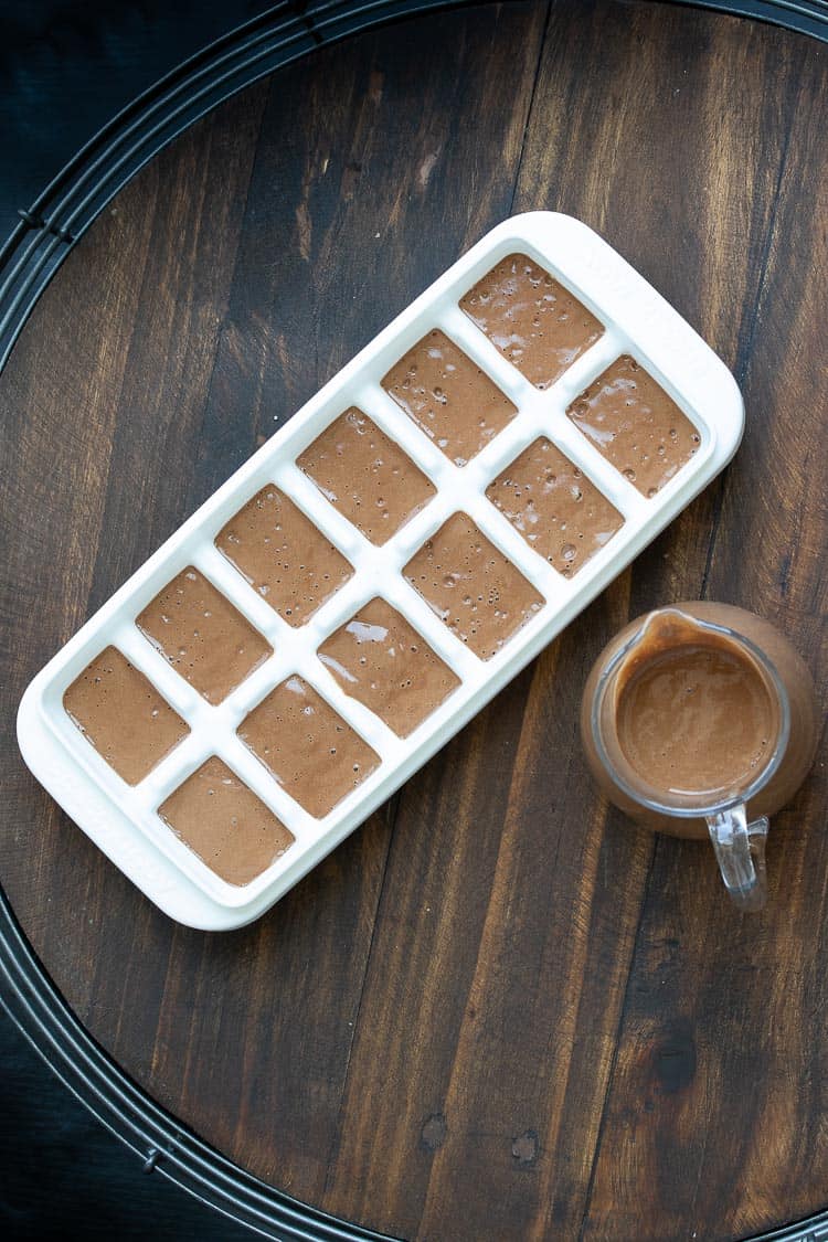 Ice cube tray filled with chocolate smoothie on a wooden table