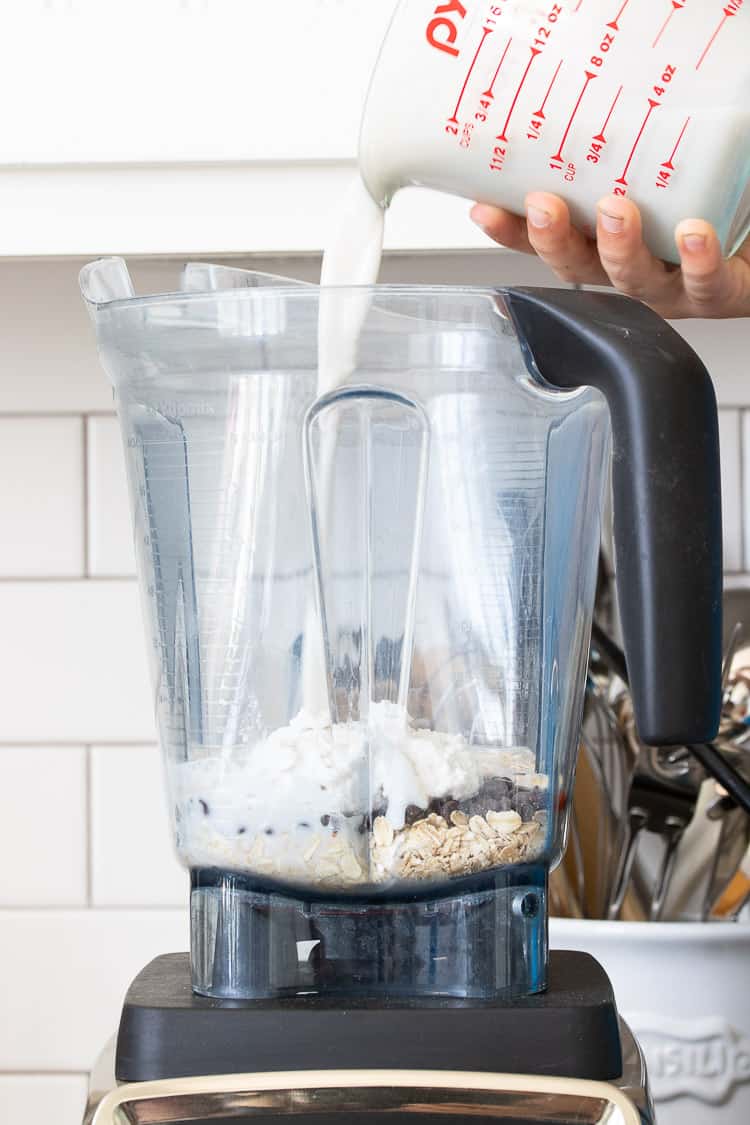 Milk being poured into a blender filled with oats, chocolate chips and coconut cream