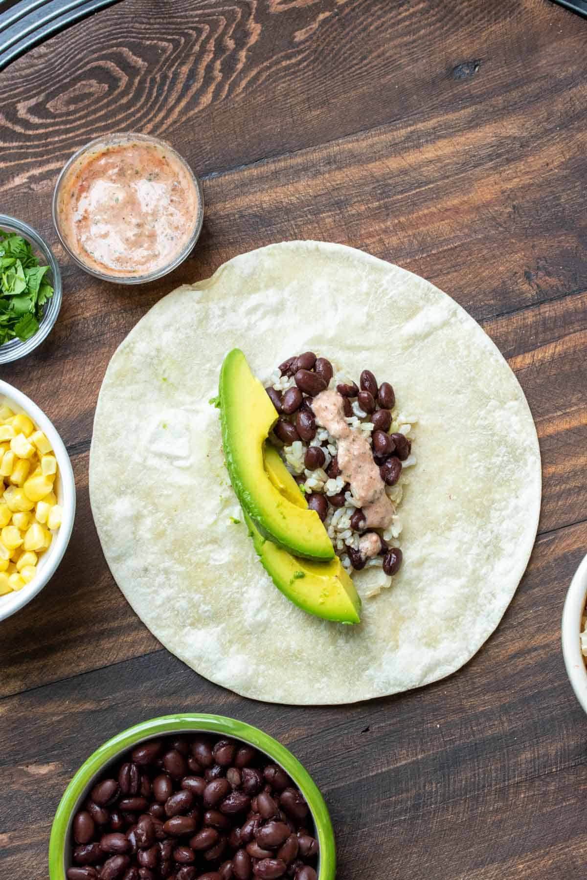 Open tortilla with avocado, beans and rice on a wooden table