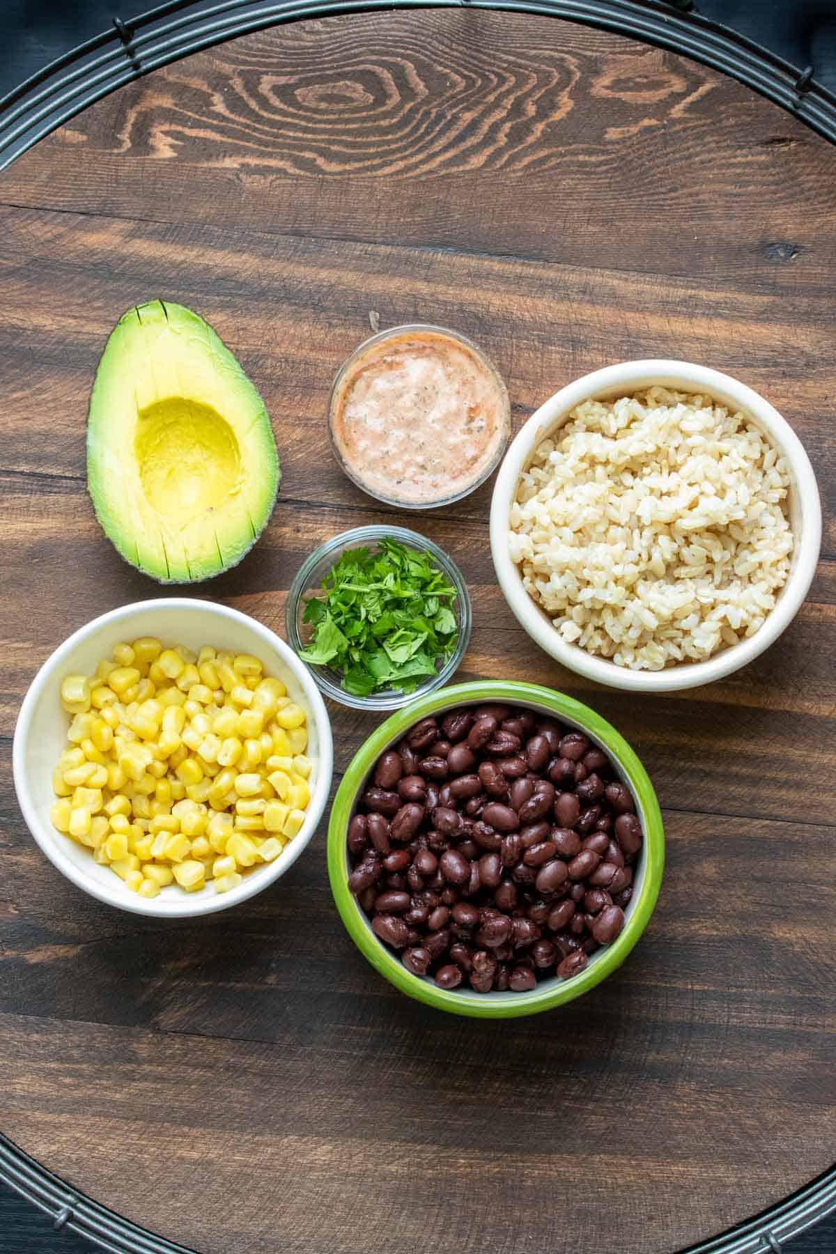 Beans, corn, rice, cilantro, creamy red sauce and half an avocado on a wooden table