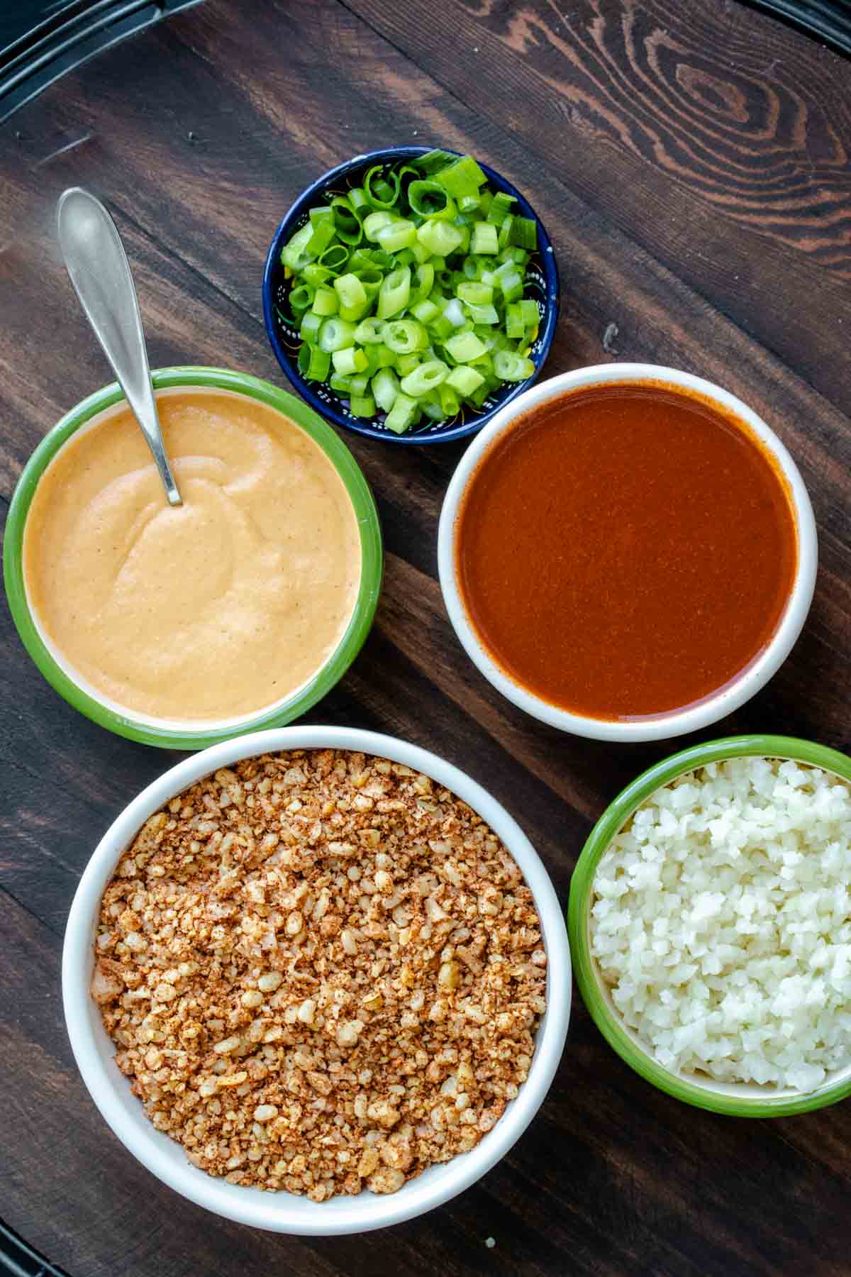 Bowls with vegan taco meat, cheese sauce, cauliflower rice, enchilada sauce and green onions