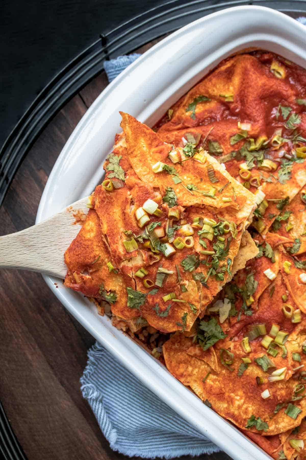 A piece of baked enchiladas being taken out of a white baking pan