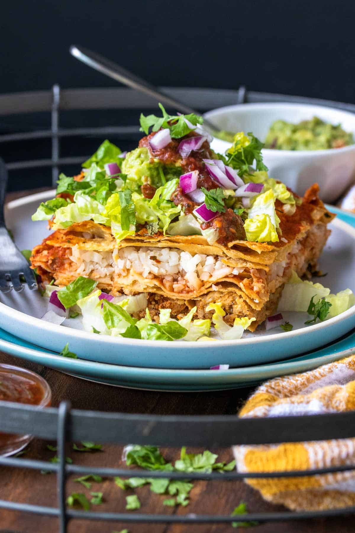 Piece of enchilada casserole topped with lettuce and red onions on a white plate.