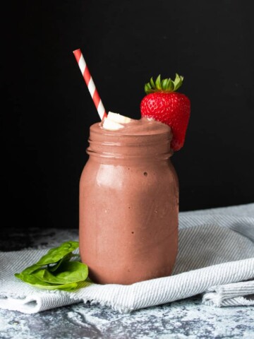 Glass jar with a reddish smoothie surrounded by pieces of strawberry, banana and spinach