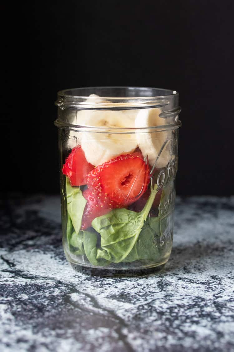 Glass jar layered with spinach, strawberries and banana slices