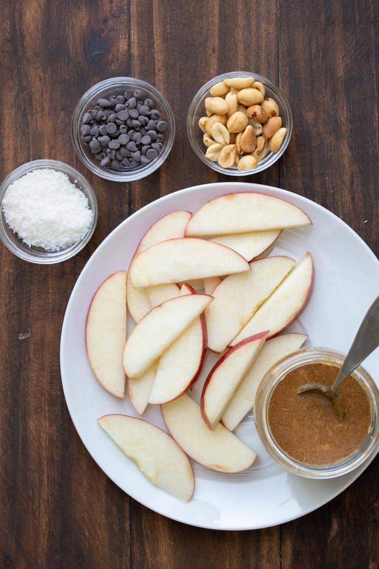 Sliced apples on a white plate surrounded by dessert nacho toppings