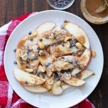 Apple nachos with caramel and toppings on a white plate