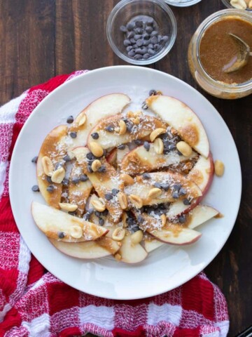 Apple nachos with caramel and toppings on a white plate