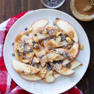 Apple nachos with caramel and toppings on a white plate