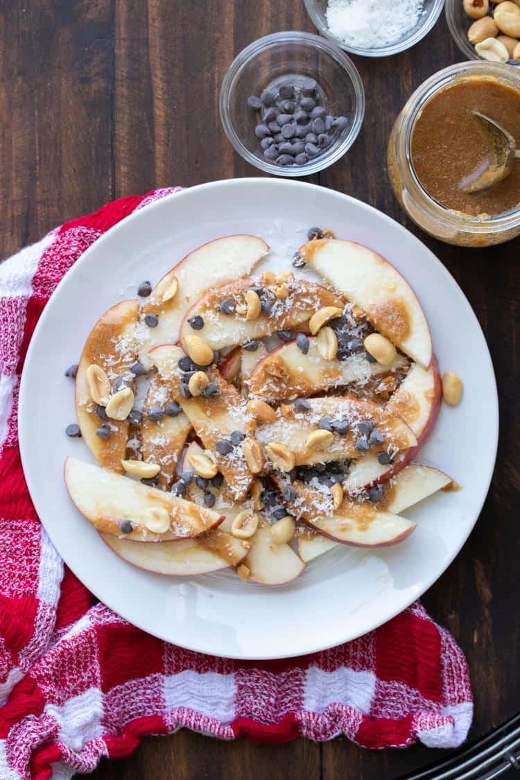 Apple nachos with caramel and toppings on a white plate