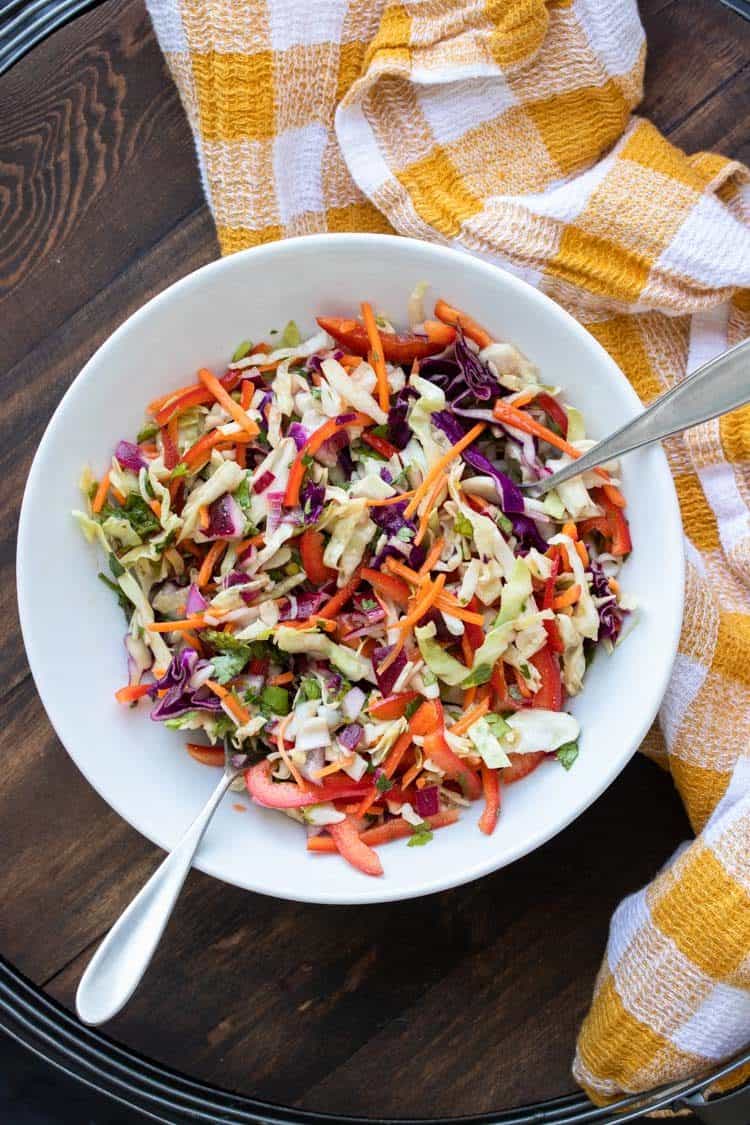 Two silver utensils in a white bowl with veggie coleslaw