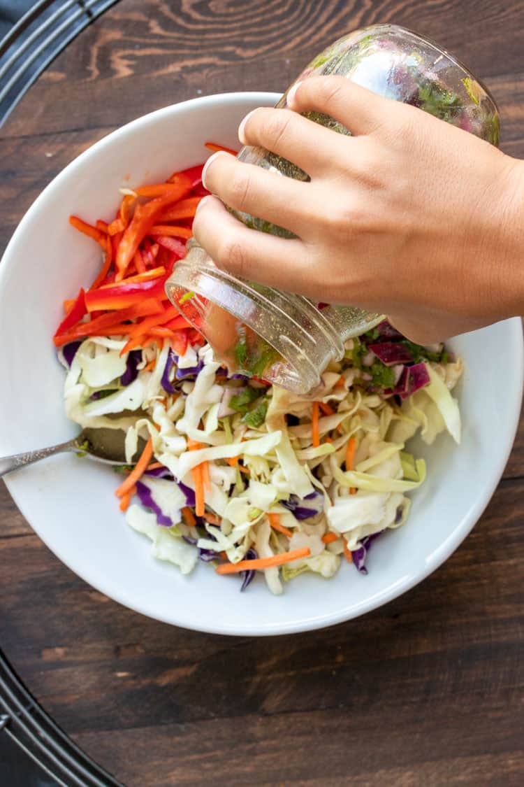 Hand pouring dressing from glass jar onto a salad