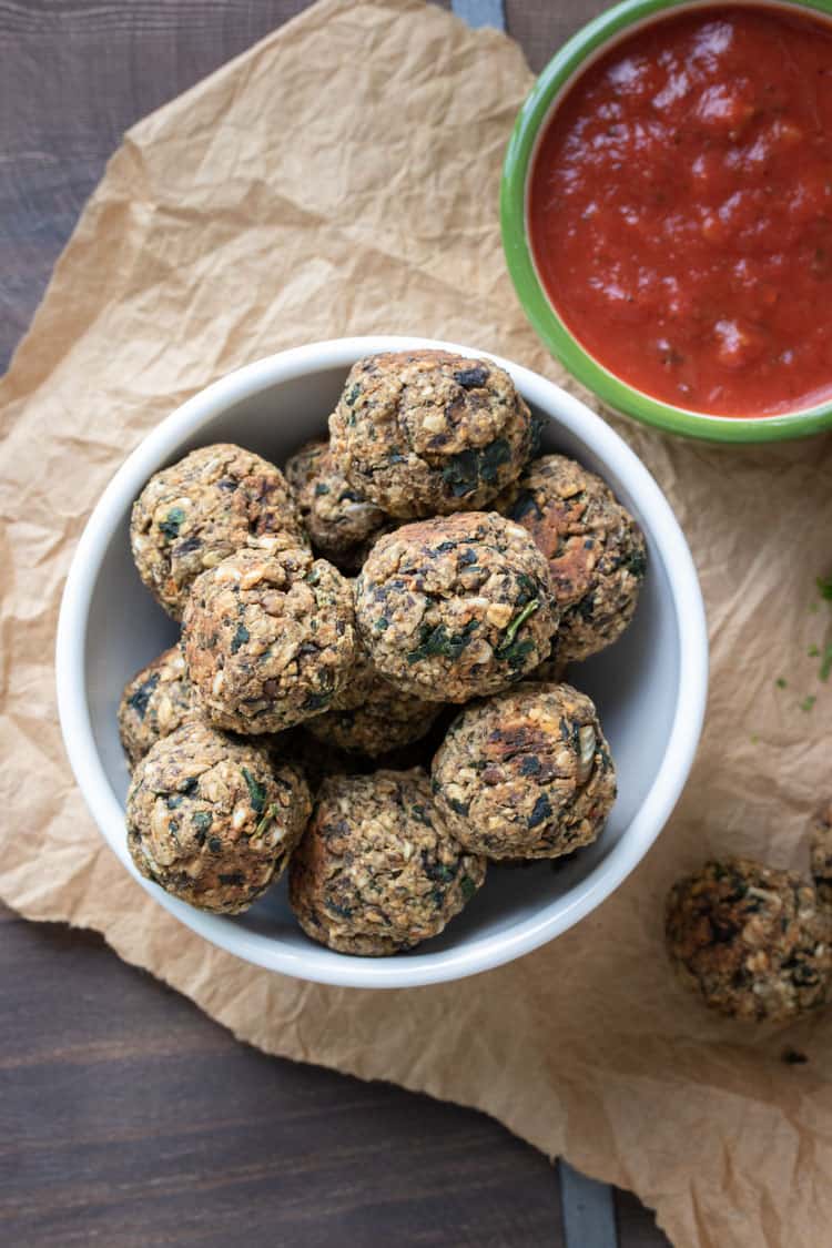 White bowl with vegan meatballs next to a bowl of marinara