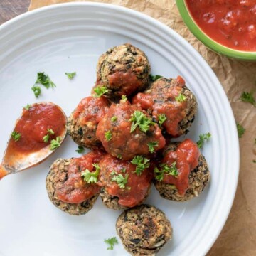 Spoon putting marinara over vegan meatballs on a white plate