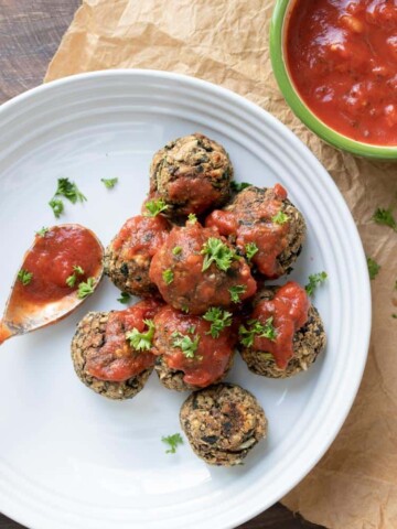 Spoon putting marinara over vegan meatballs on a white plate