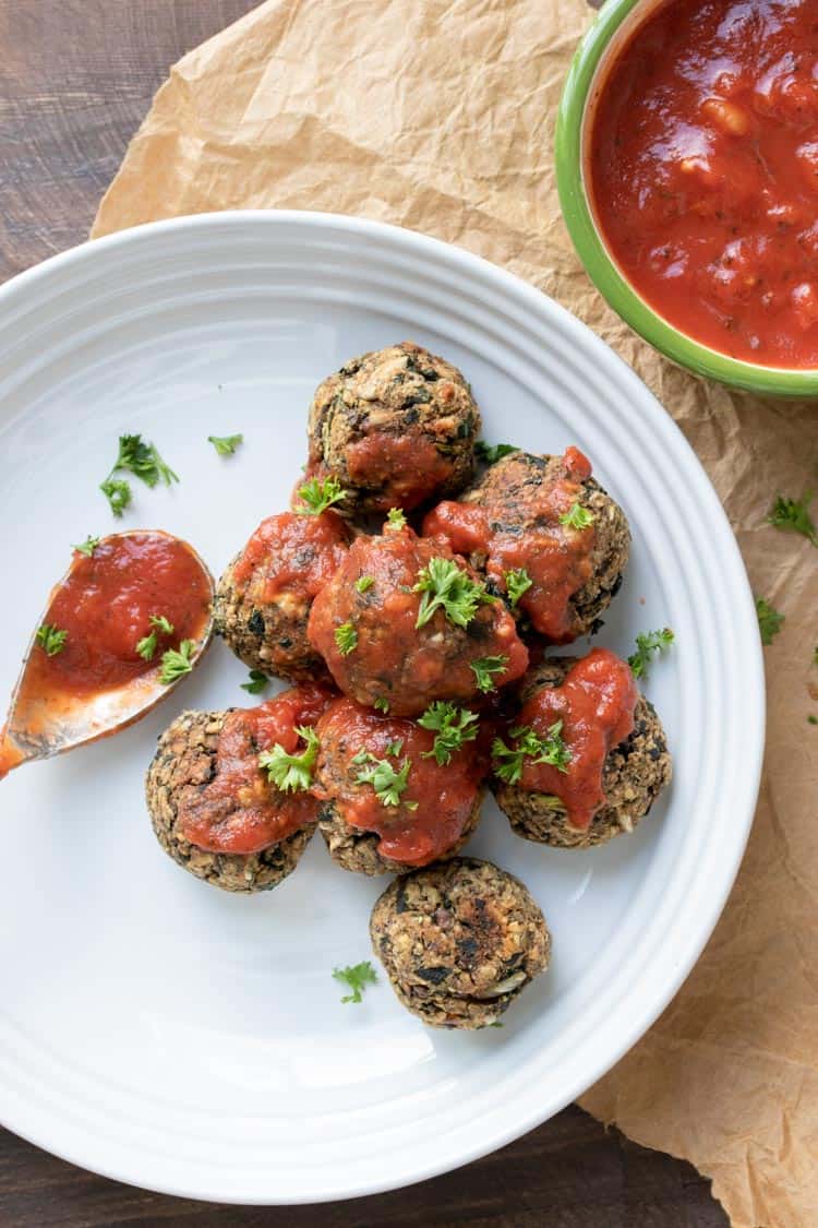 Spoon putting marinara over vegan meatballs on a white plate