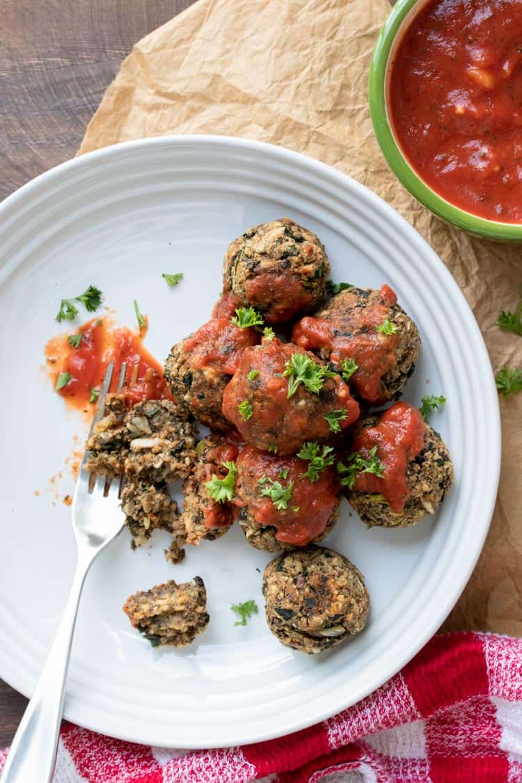 Fork taking a bite of vegan meatballs with marinara on a white plate