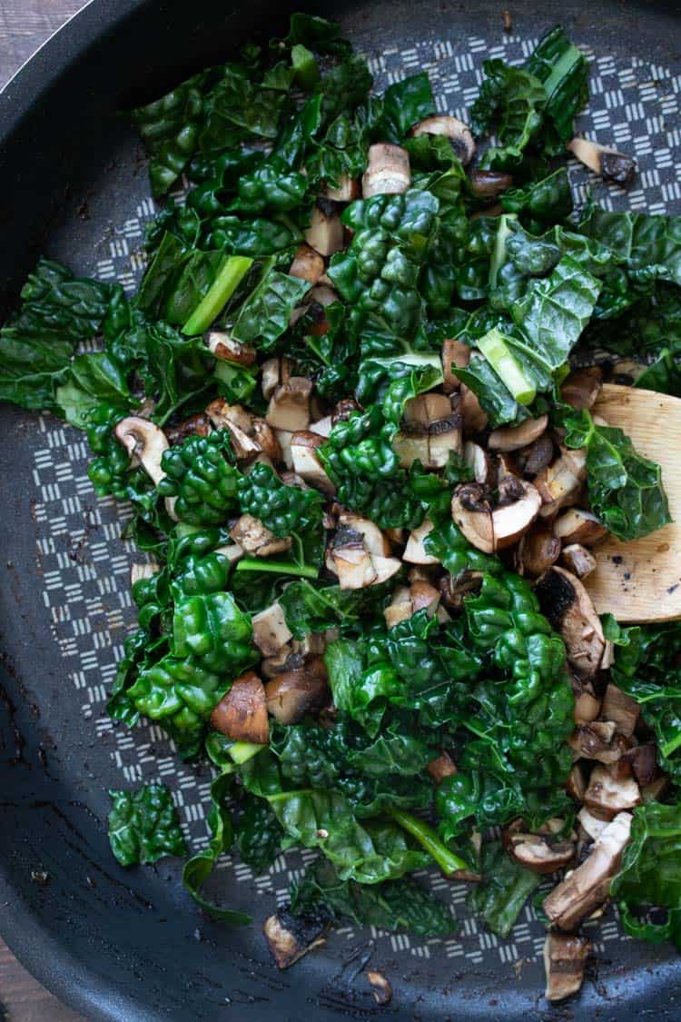 Spoon sautéing kale and mushrooms in a pan