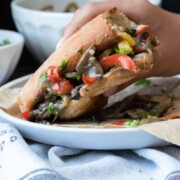 Hand holding a half eaten mushroom Philly cheesesteak sandwich.