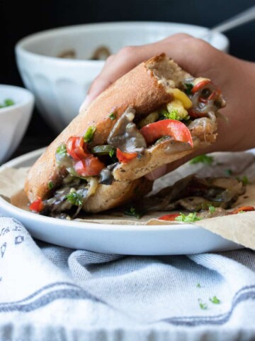 Hand holding a half eaten mushroom Philly cheesesteak sandwich.