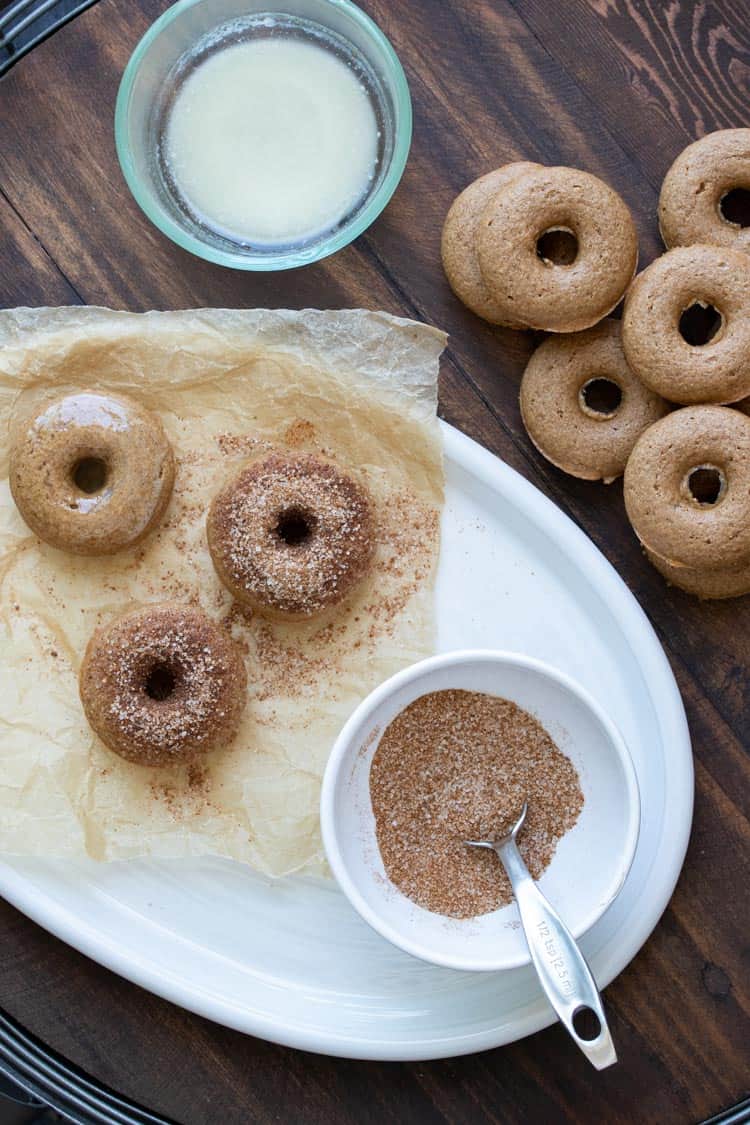 Baked donuts on a white plate being coated in a cinnamon and sugar topping