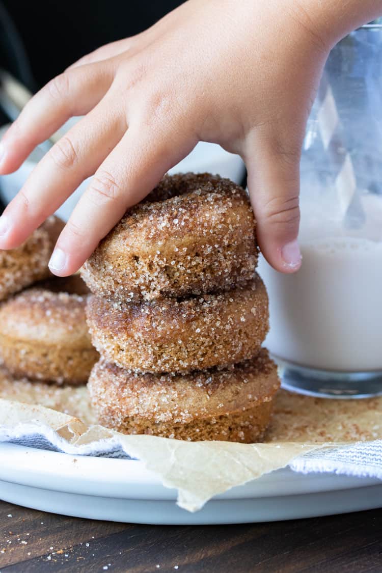 Child's hand grabbing the top cinnamon sugar donut from a stack of three