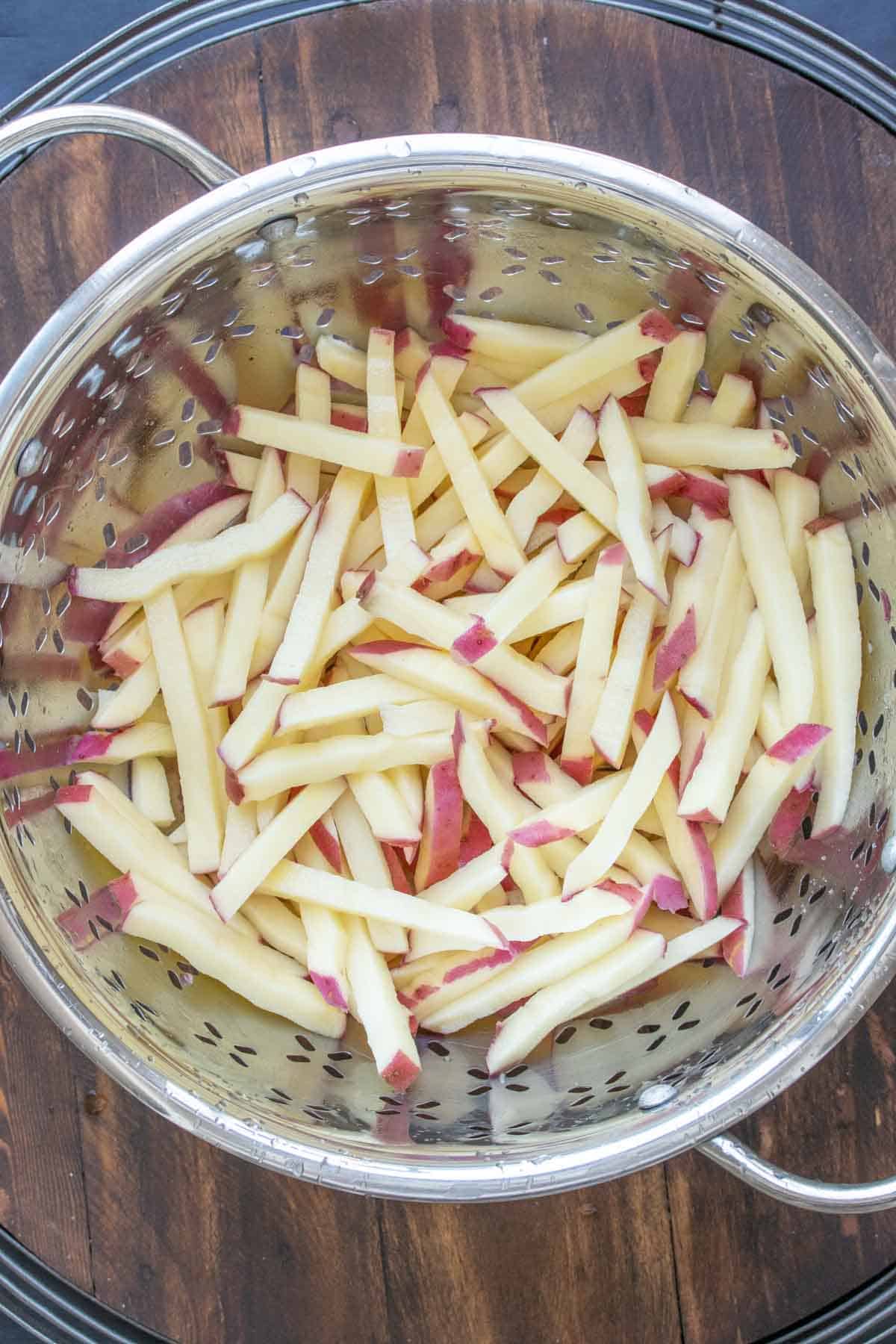 Raw french fries drying in a stainless steel colander.