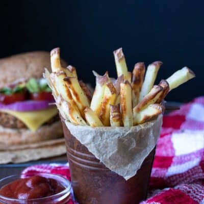 Brown pail on a red checkered towel filled with crispy french fries next to ketchup
