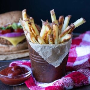 Crispy baked french fries in a brown tin on a red checkered towel.