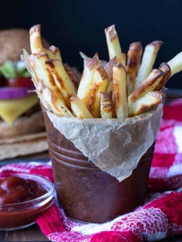 Crispy baked french fries in a brown tin on a red checkered towel.