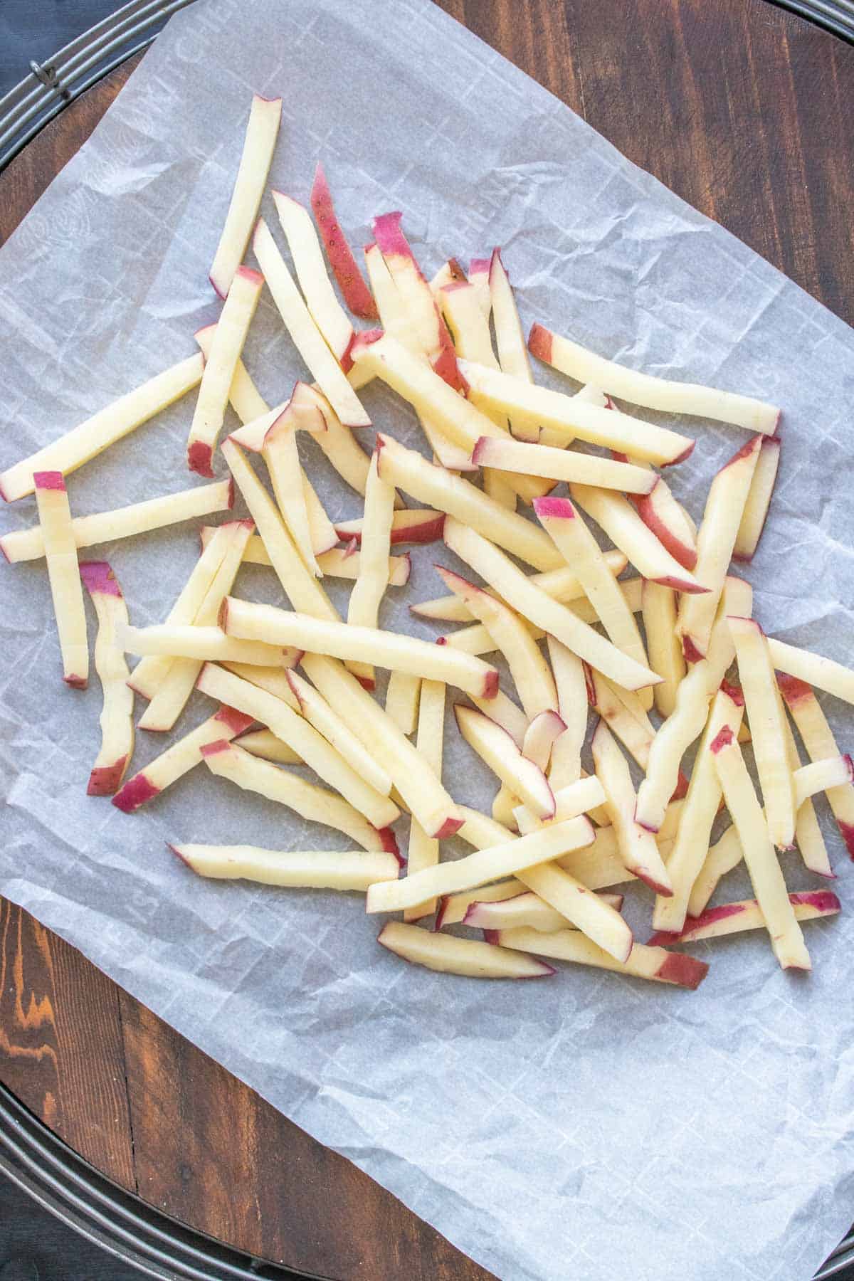Raw potatoes cut into matchstick slices on a piece of parchment.