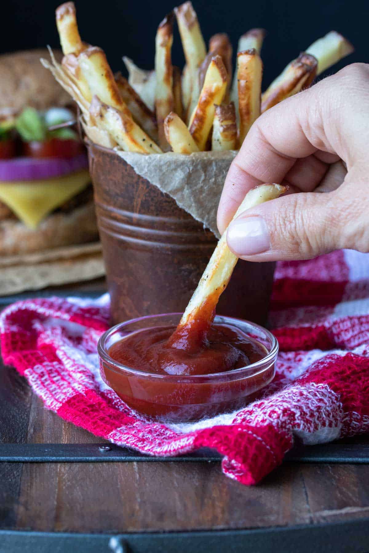Hand dipping a french fry in a small glass bowl of ketchup