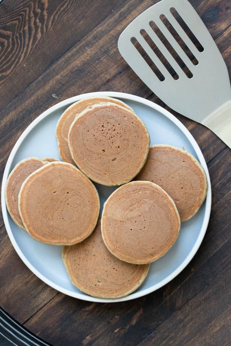 Grey plate with a pile of pancakes next to a metal spatula
