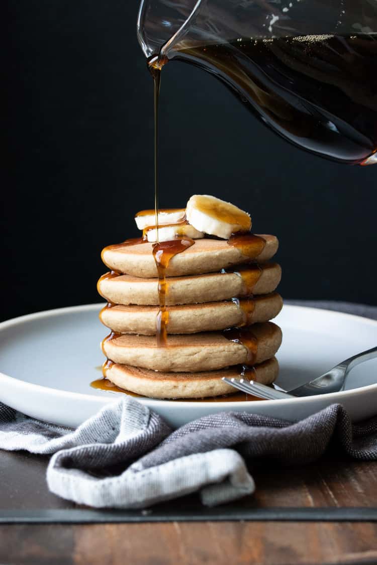 Glass carafe pouring maple syrup on a stack of pancakes