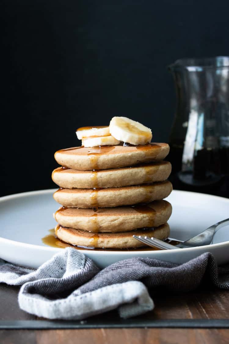 Stack of five pancakes with maple syrup and slices of banana on top