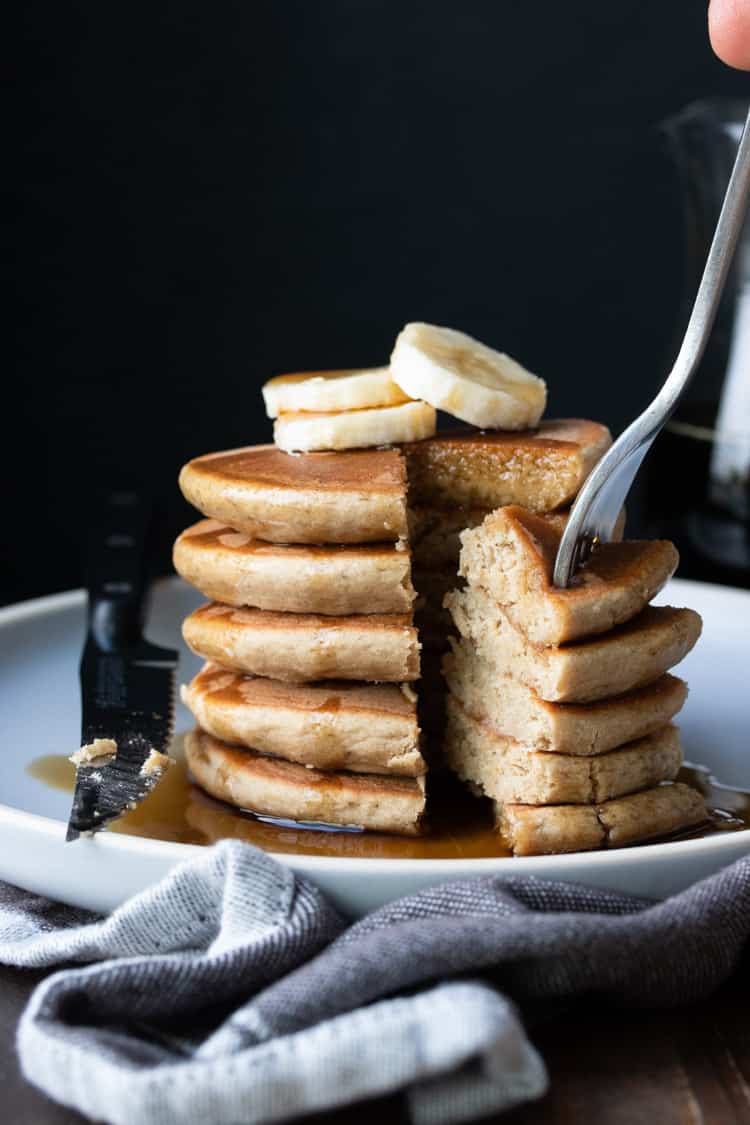 Fork taking a bite of pancakes with banana slices and maple syrup on top