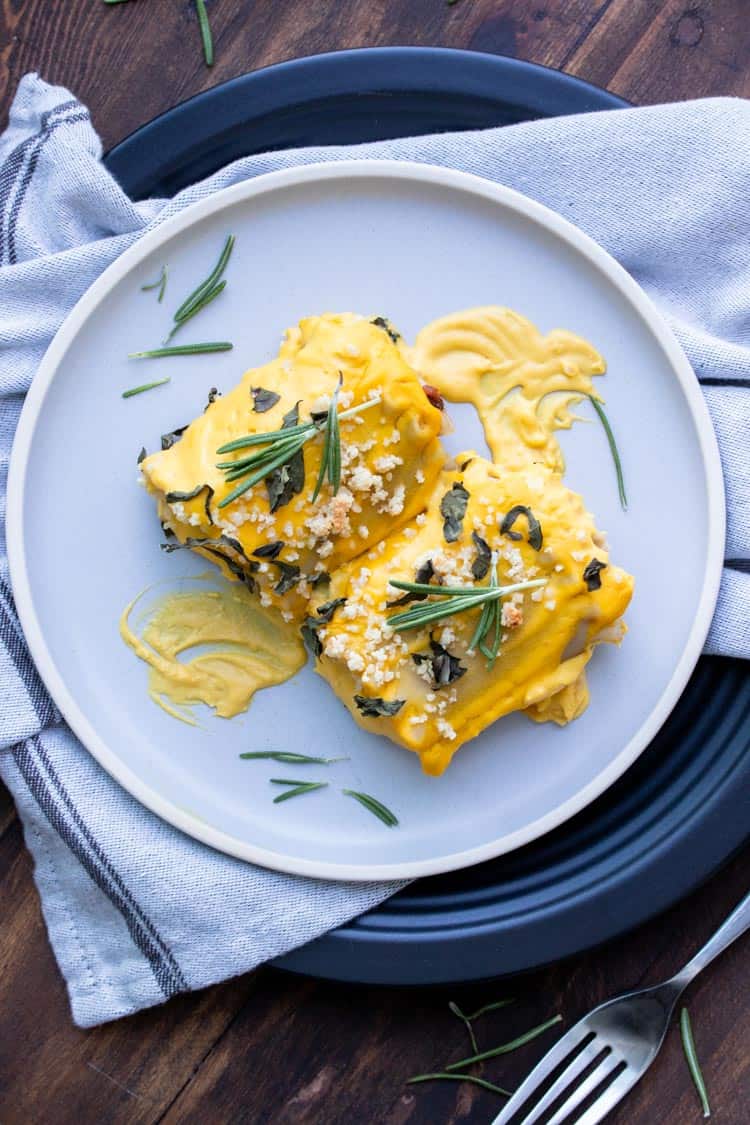 Two butternut squash lasagna roll ups topped with rosemary on a grey plate