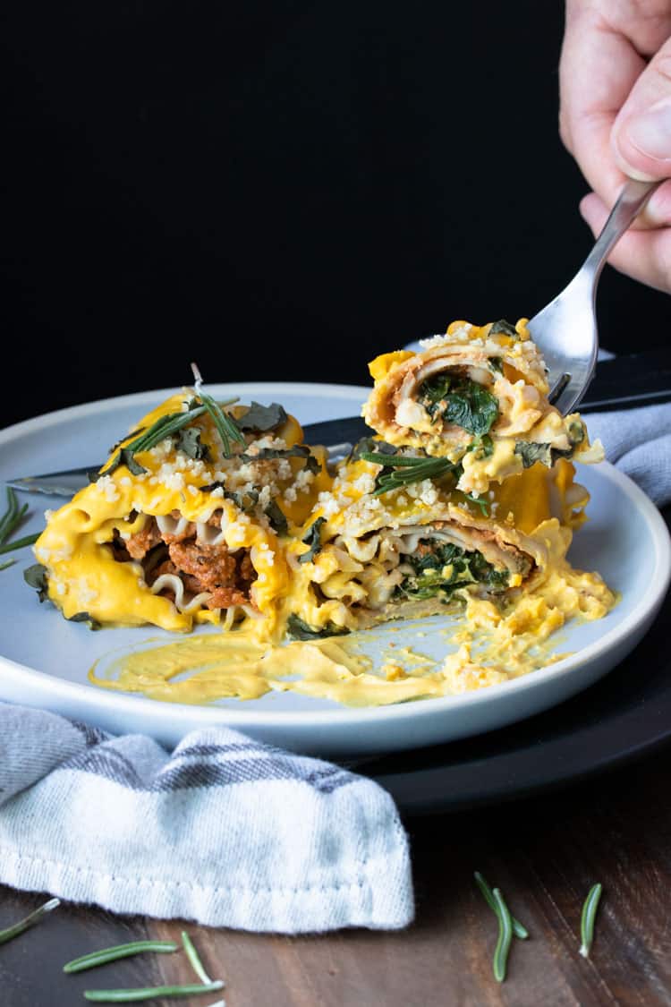 Fork taking a bite of butternut squash lasagna roll ups filled with sun dried tomato ricotta